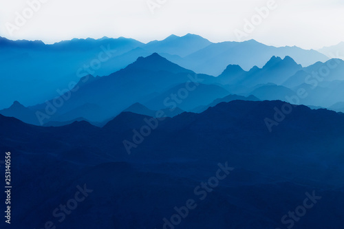 Beautiful view from the mountain. Panorama. Mountain range with visible silhouettes through the morning blue fog.