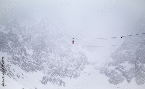 Red single gondola, cable car going up to the top of the high mountain peak in the winter season in Tatrzanska Lomnica , Slovakia