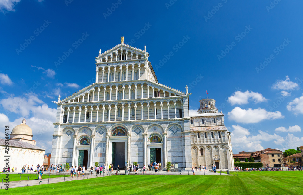 Pisa Cathedral Duomo Cattedrale and Leaning Tower Torre on Piazza del Miracoli square green grass lawn, blue sky with white clouds background in sunny day, Tuscany, Italy