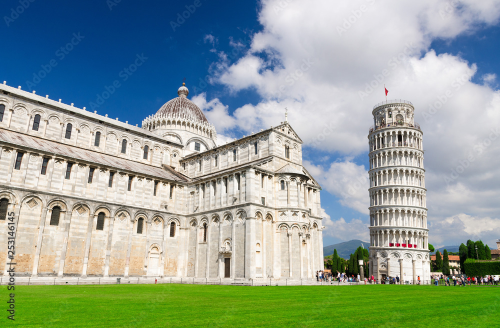 Pisa Cathedral Duomo Cattedrale and Leaning Tower Torre on Piazza del Miracoli square green grass lawn, blue sky with white clouds background in sunny day, Tuscany, Italy