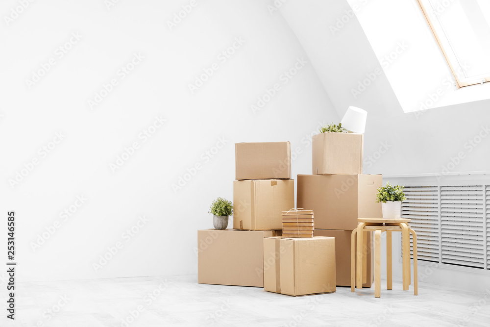 Moving to a new home. Belongings in cardboard boxes, books and green plants in pots stand on the gray floor against the background of a white wall. Moving to a new home. Belongings in cardboard boxes, books and green plants in pots stand on the gray floor against the background of a white wall.