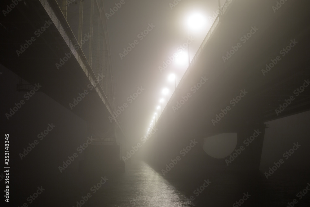 A mysterious evening fog above the river in big city. Bridge in the mist, cold weather scenery. Soft, blurry, misty look. Colorful, mystic industrial cityscape. A mysterious evening fog above the river in big city. Bridge in the mist, cold weather scenery. Soft, blurry, misty look. Colorful, mystic industrial cityscape.