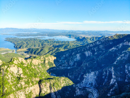 Aerial view of mountain with water reservoir on the background. Mountain peak with beautiful blue sky and green forest. Landscape of mountain in natural reserve park. Miyun, Beijing, China.