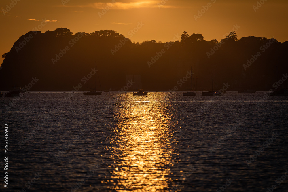 Naklejka premium Sunset reflecting on waves and boats in harbour
