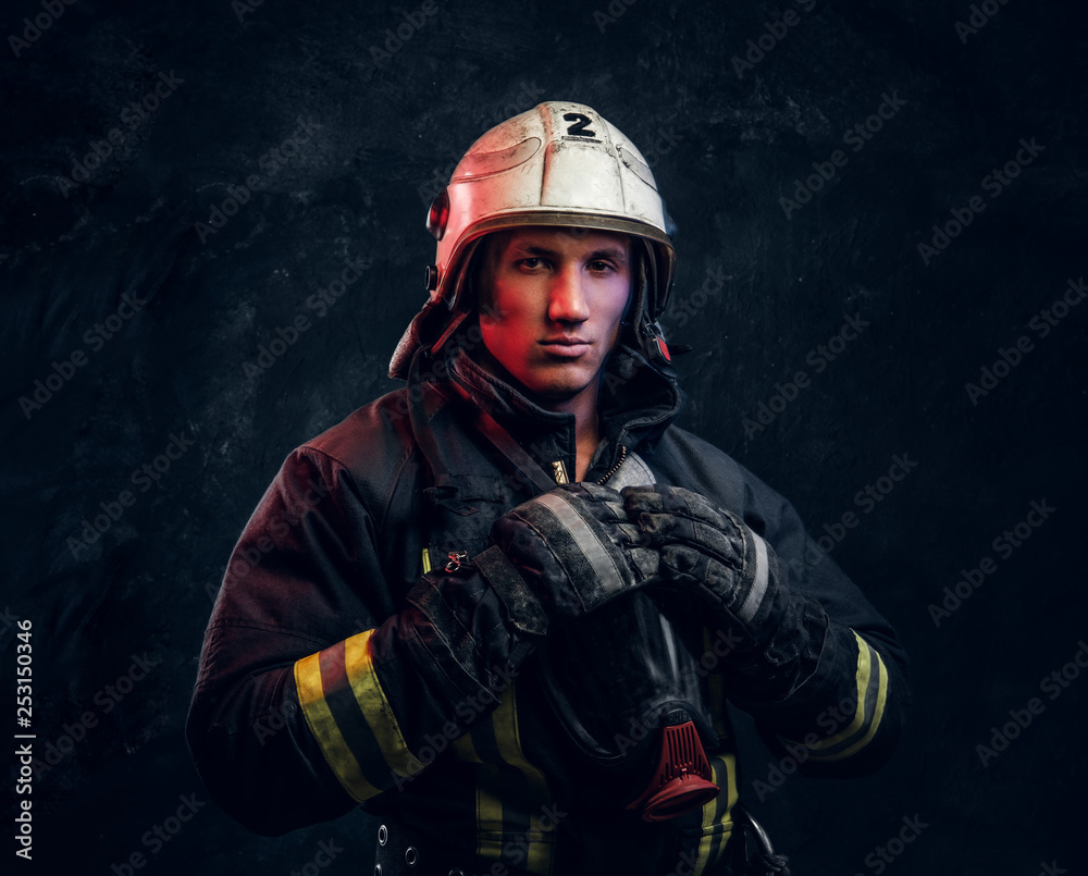 Firefighter in uniform and safety helmet posing in a dark studio, looking at the camera with a confident look. Firefighter in uniform and safety helmet posing in a dark studio, looking at the camera with a confident look.