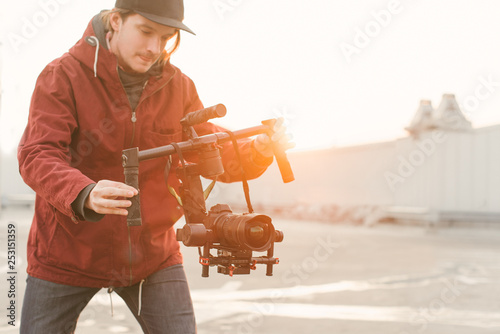 Cameraman with a stabilizer in his hands shoots a video on the dslr camera on the background of the sunset. Backstage concept photo