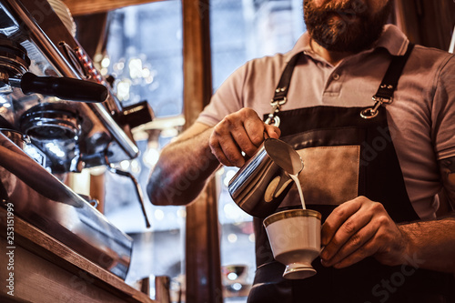 Barista in apron making a cappuccino, pouring milk in a cup in a restaurant or coffee shop