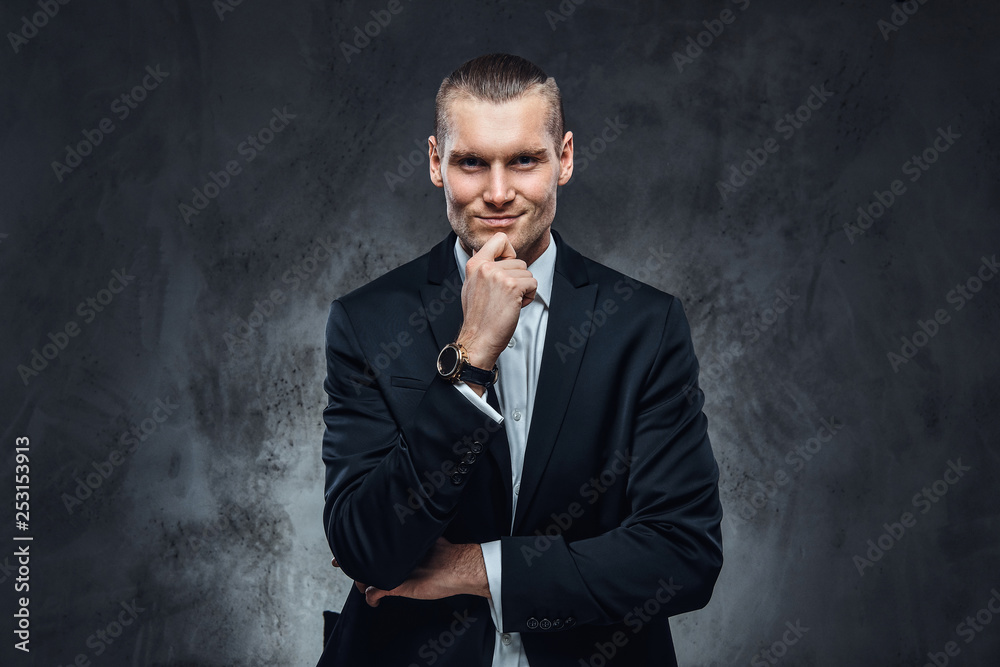 Pensive elegantly dressed handsome man wearing a black classical suit, touching his face and looking at a camera. Studio shot on a dark textured wall Pensive elegantly dressed handsome man wearing a black classical suit, touching his face and looking at a camera. Studio shot on a dark textured wall