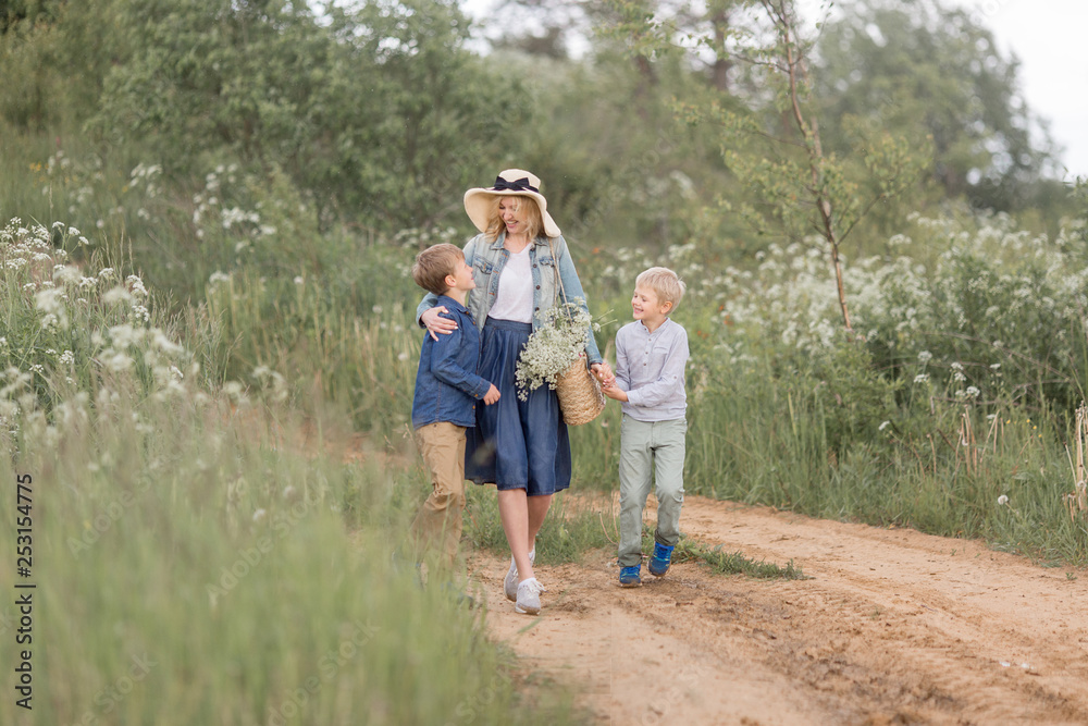 Mother in a straw hat, denim dress with young sons walking through the woods .Outdoor spring leisure concept