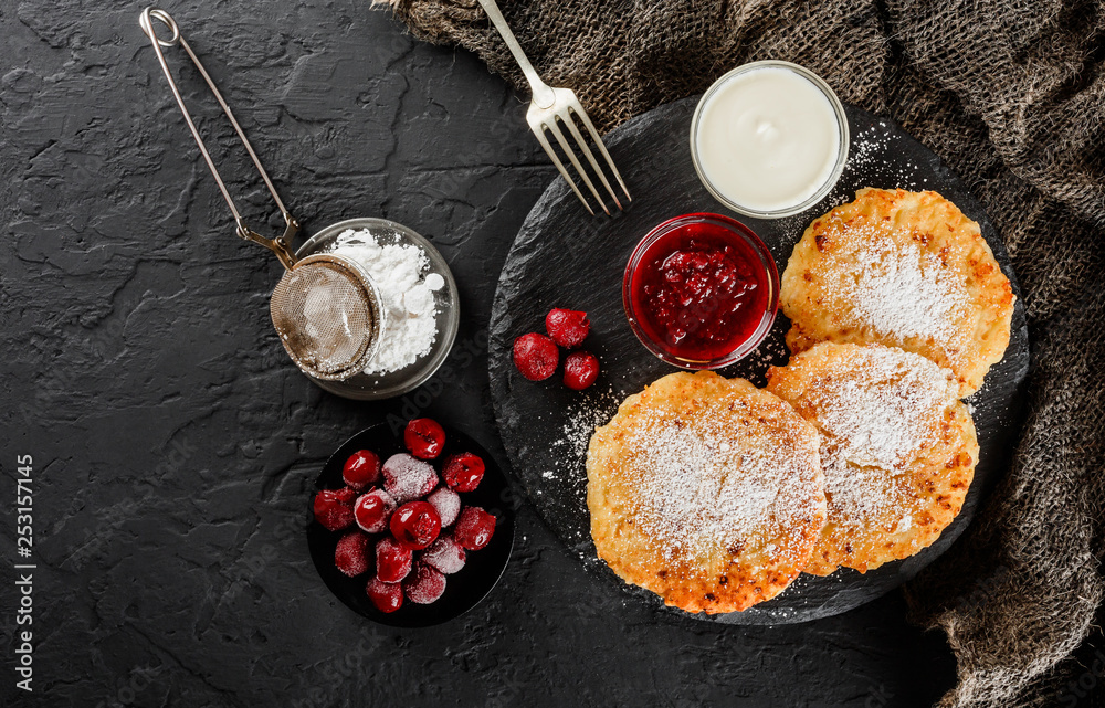 Pancakes with fruit jam, cherries, sour cream and icing sugar on black slate over dark background. Traditional Russian cuisine at the Pancake week or Shrovetide. Healthy breakfast. Top view Pancakes with fruit jam, cherries, sour cream and icing sugar on black slate over dark background. Traditional Russian cuisine at the Pancake week or Shrovetide. Healthy breakfast. Top view