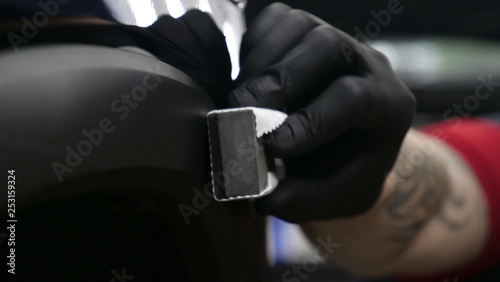 A professional worker guy (Male) applies ceramics (special liquid) to the car using an applicator (sponge) in black gloves and in a protective robe. Concept of: Auto service, Deteyling. © dkHDvideo