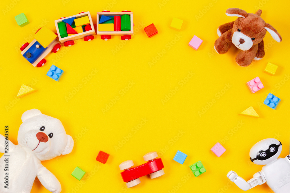 Kids toys background. White teddy bear, wooden train, toy car, robot, colorful blocks on yellow background - obrazy, fototapety, plakaty 