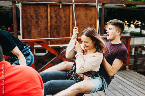 Young cute extreme couple rope sliding and gaining speed on the ropeway where girl is laughing with fear and man is screaming both holding by rope slide cable.