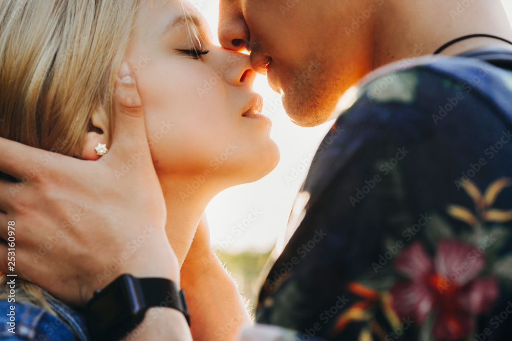Close up portrait of a cute young caucasian blonde couple trying to kiss  where man is holding his girlfriend face in his hands close outside while  dating. Stock Photo