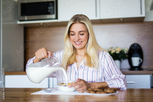 healthy breakfast - blondie girl pouring milk in bowl with corn flakes in modern kitchen