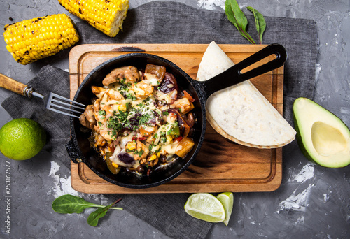 Mexican dish fajitas with meat, bell pepper, onion in a pan on a wooden board on a concrete gray background photo