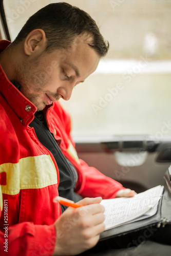 Young handsome paramedic in his ambulance smiling and writing report.