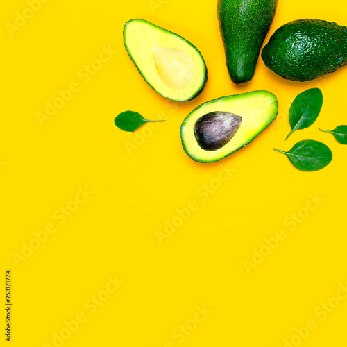 Ripe sliced avocado and spinach leaves on yellow background top view. Creative food composition Flat lay. Pop art design, tropical summer abstract background with avocado. Green avocadoes pattern