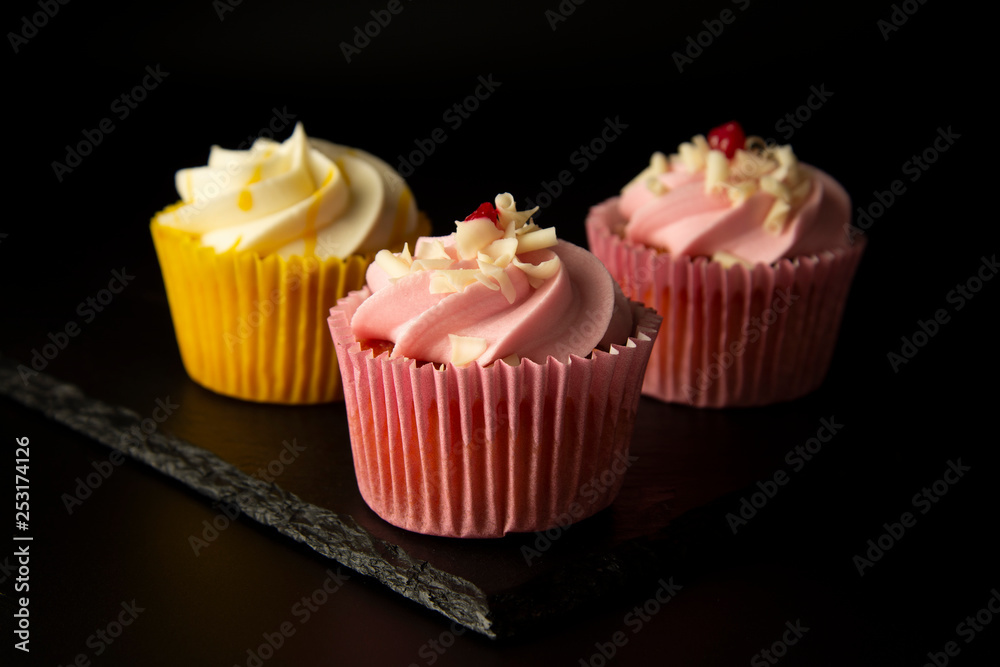 Pink and yellow cupcakes against a black background, birthday or party cupcakes. Party sweet food, desserts. Copy space.