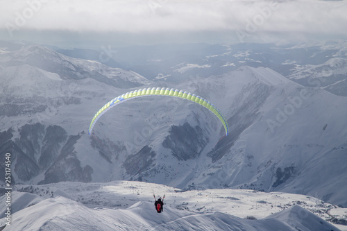 Paralotniarstwo w zaśnieżonych górach nad ośrodkiem narciarskim w słoneczny zimowy dzień. Góry Kaukazu. Gruzja, region Gudauri.
