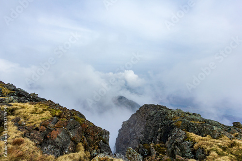 A view from a mountain summit with an other summit and altitude white clouds © Dolwolfian