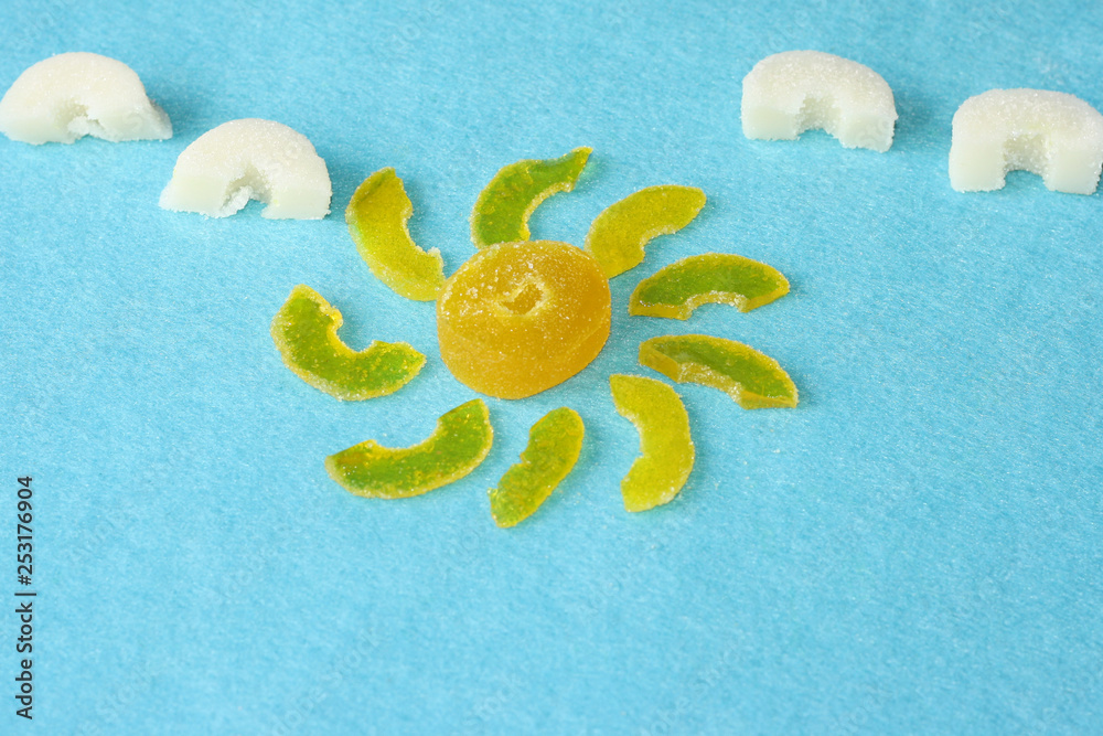 Sun from yellow marmalade with rays and white marmalade clouds on a blue felt background. Multicolored chewy candy. Sweets and pleasures, treats. Sun from yellow marmalade with rays and white marmalade clouds on a blue felt background. Multicolored chewy candy. Sweets and pleasures, treats.