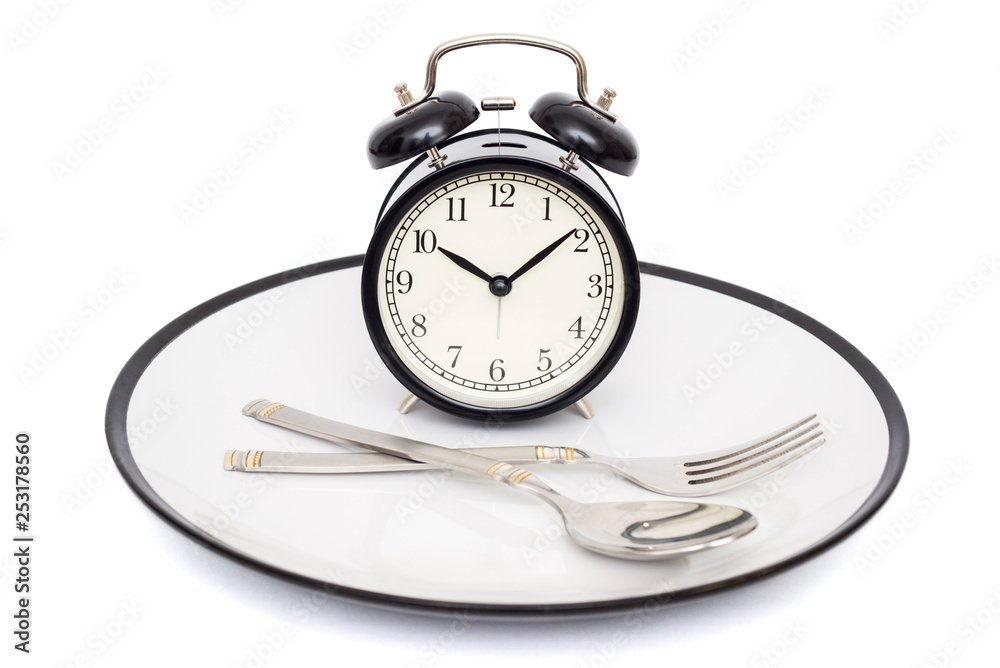 Black alarm clock with fork and knife on the plate. Isolated on white. Time to eat. Weight loss or diet concept Black alarm clock with fork and knife on the plate. Isolated on white. Time to eat. Weight loss or diet concept