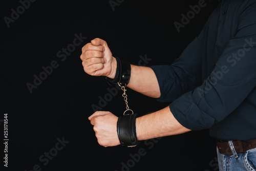 men's hands chained in leather handcuffs on black background