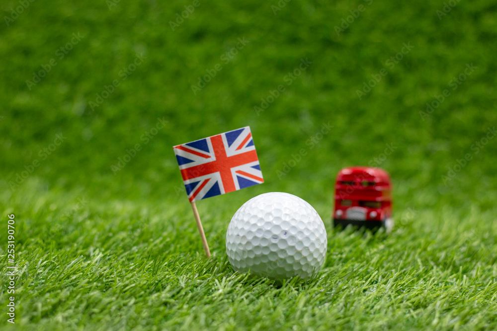 Obraz premium Golf ball with Union Jack flag with double decker bus on green grass