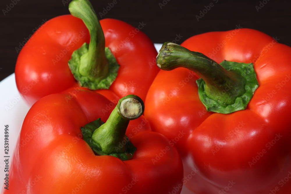 Three large red peppers lie on a white serving plate, standing on a table with a dark background.