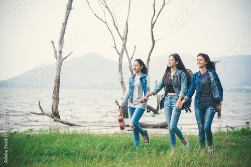 A group of young women who are walking hand in hand on green grass near the lake.