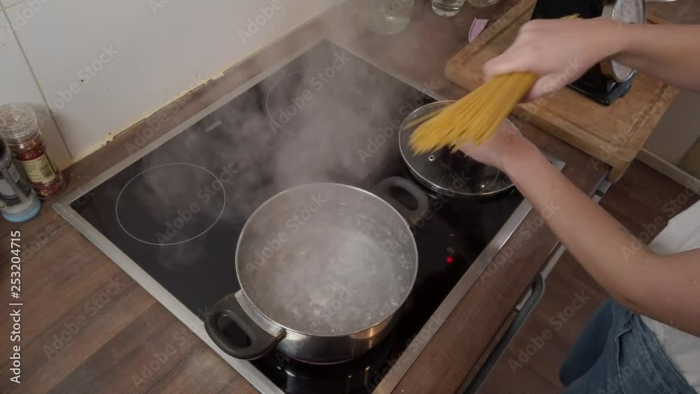 Young woman puts spaghetti into boiling water for cooking Young woman puts spaghetti into boiling water for cooking