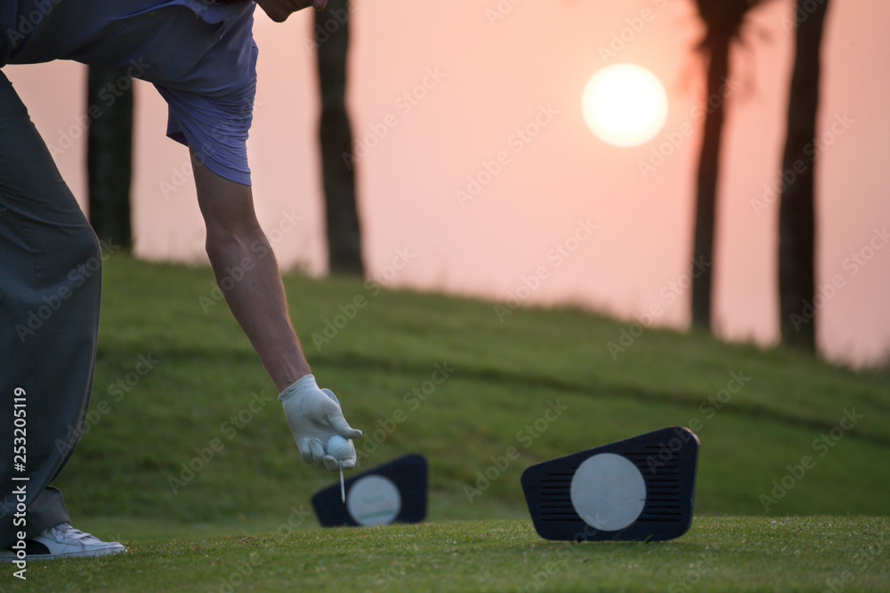 Obraz premium Golfers are putting golf ball on the teeing ground at the starting point. There is a sunrise on the background.