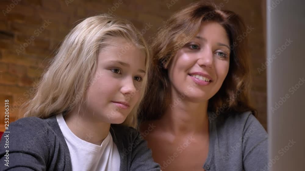Closeup portrait of young mother and small pretty girl watching a movie on the laptop together. Mom petting her daughter with tenderness Closeup portrait of young mother and small pretty girl watching a movie on the laptop together. Mom petting her daughter with tenderness