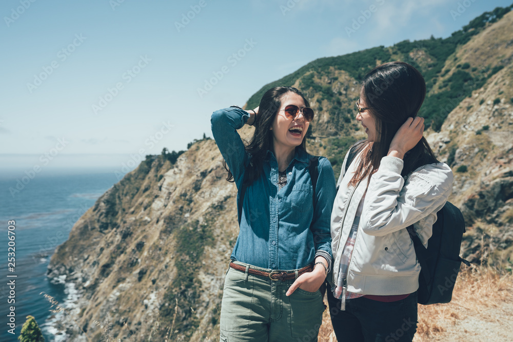 asian girl friends on hiking trip in mountains walking along Pacific Ocean coastline Big Sur California USA. cheerful sisters happy laughing having fun chatting outdoors while travel together spring.