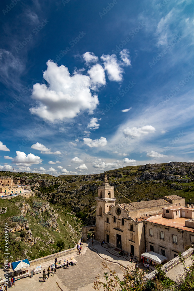 MATERA, ITALY - AUGUST 27, 2018: High angle summer day panoramic view over Church of Saint Peter or Chiesa di San Pietro Caveoso with white puffy clouds moving on the Italian blue sky