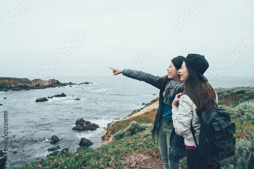 Beautiful spring coastal landscape. sister on hiking trip resting on top of mountain looking at Pacific Ocean Big Sur California USA. friends backpackers pointing finger showing sharing view