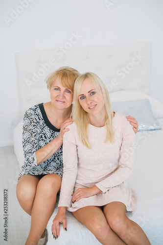 Obraz na płótnie Two beautiful women a mother and daughter sitting on the bed in white room w salonie