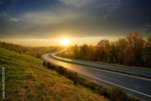 Obraz na płótnie Sunset over empty asphalt highway winding through autumn landscape w salonie