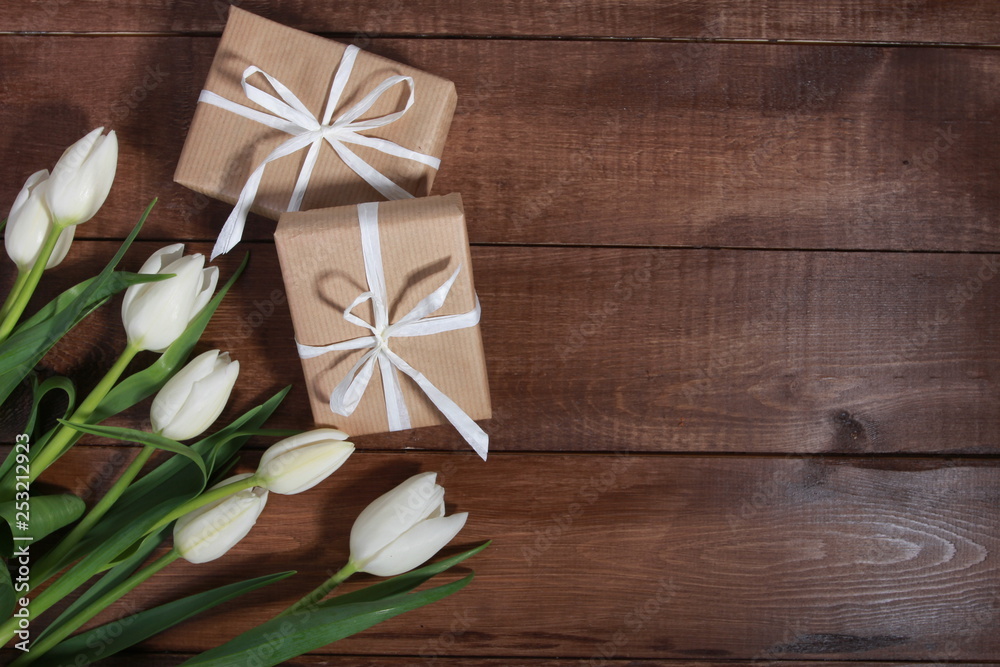 White tulips and gift boxes on brown wooden table. Women day concept. White ribbon, craft wrap, 8 march, spring White tulips and gift boxes on brown wooden table. Women day concept. White ribbon, craft wrap, 8 march, spring