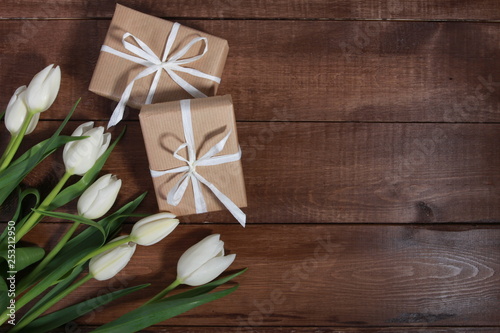 White tulips and gift boxes on brown wooden table. Women day concept. White ribbon, craft wrap, 8 march, spring