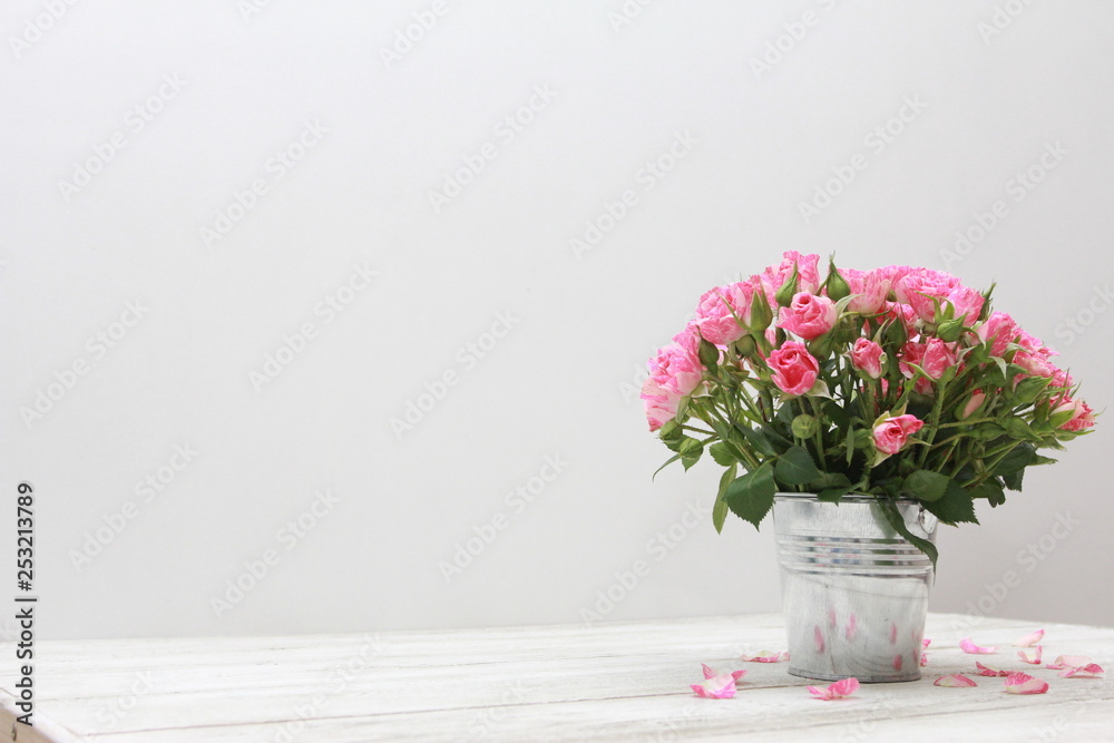 Bunch of roses in tin bucket and petals on white wooden table. Women day concept. Spring, blooming, 8 march, birthday