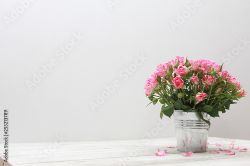 Bunch of roses in tin bucket and petals on white wooden table. Women day concept. Spring, blooming, 8 march, birthday