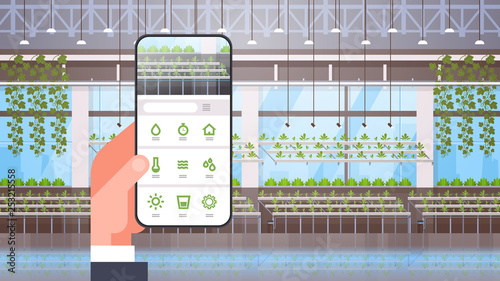 hand holding smartphone using smart control farming system mobile application organic hydroponic green plants row cultivation farm modern greenhouse interior horizontal