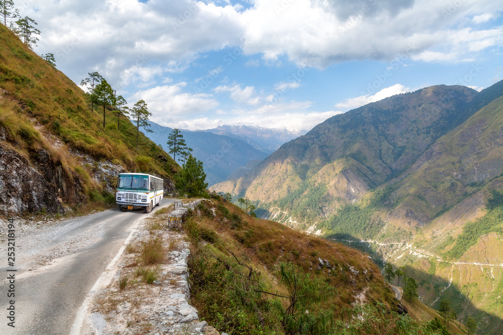 Tourist bus on mountain road with distant Himalaya snow peaks and scenic mountain valley near Munsiyari Uttarakhand India.
