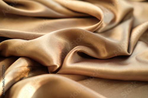 The gold fabric is laid out waves. Satin fabric. Brown material textile.