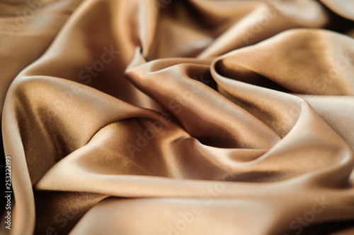 The gold fabric is laid out waves. Satin fabric. Brown material textile.
