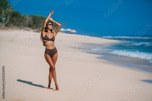 Beautiful tanned girl posing on beach with white sand and blue ocean.