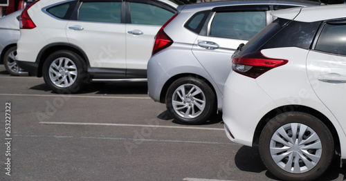 Closeup of back or rear side of white car and other cars parking in outdoor parking area in sunny day. 