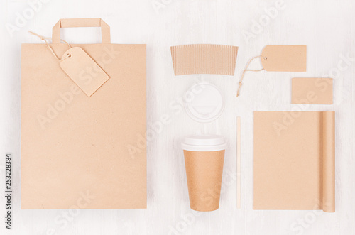 Coffee shop template for branding identity - brown paper cup with blank notebook, bag, label, card, cap on white wood board, top view.